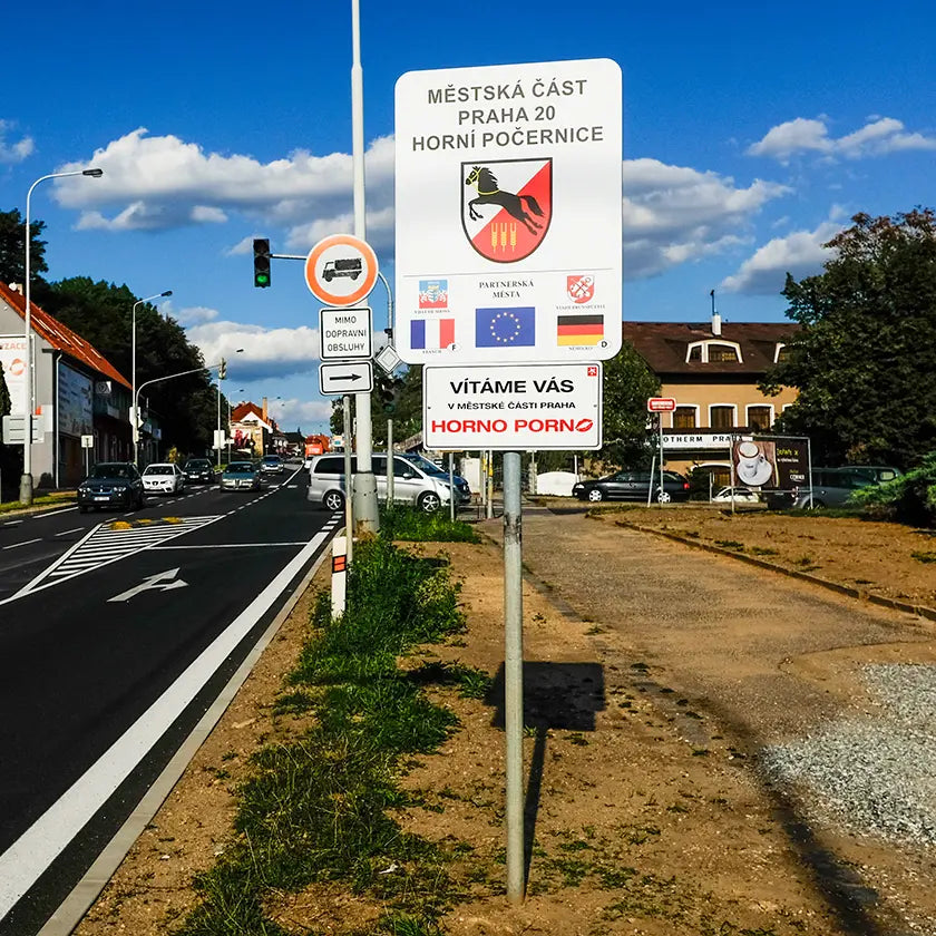 Vjezd do Horních Počernic – Náchodská ulice ve směru od Černého Mostu; u silnice stojí uvítací cedule s nápisem "Vítáme vás v městské části HornoPorno".